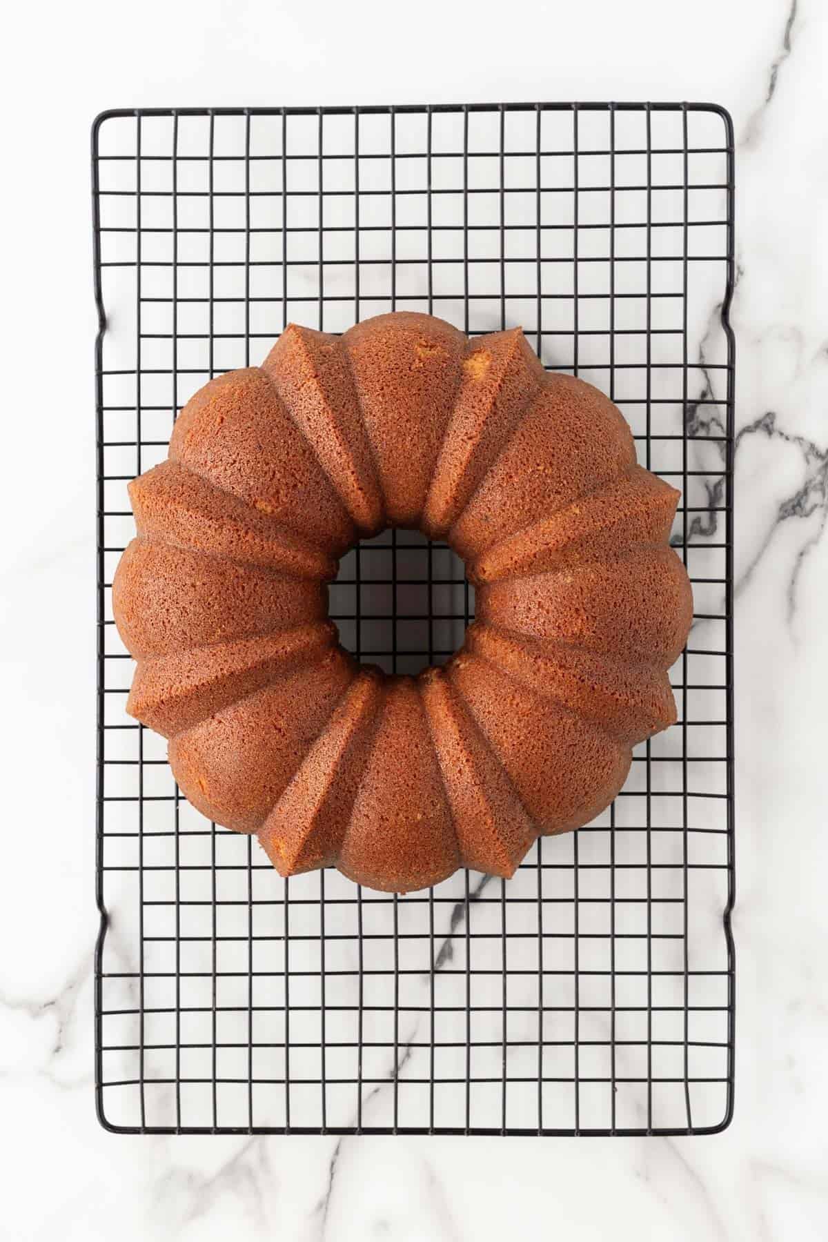 Freshly baked creamsicle pound cake cooling on a black wire rack over a white marble surface
