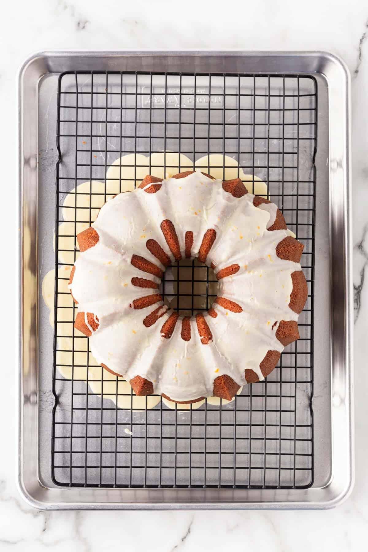 Glazed creamsicle pound cake resting on a wire rack set inside a sheet pan with excess glaze dripping below