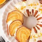 Overhead shot of sliced creamsicle pound cake with orange glaze and fresh zest on a white serving platter with orange halves nearby