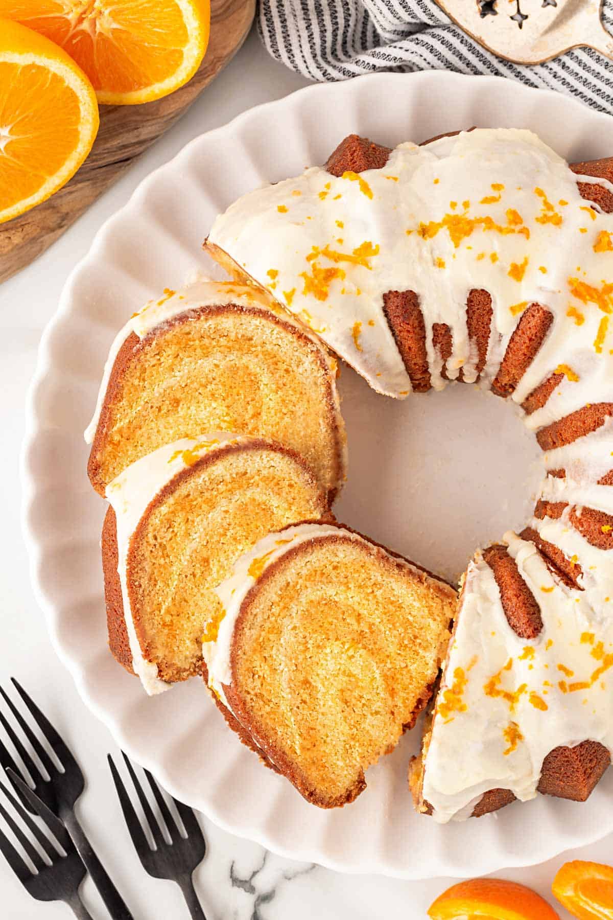 Overhead shot of sliced creamsicle pound cake with orange glaze and fresh zest on a white serving platter with orange halves nearby