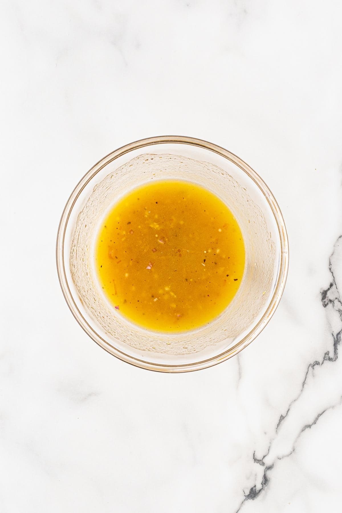 Citrus vinaigrette in a clear glass bowl on a white marble countertop