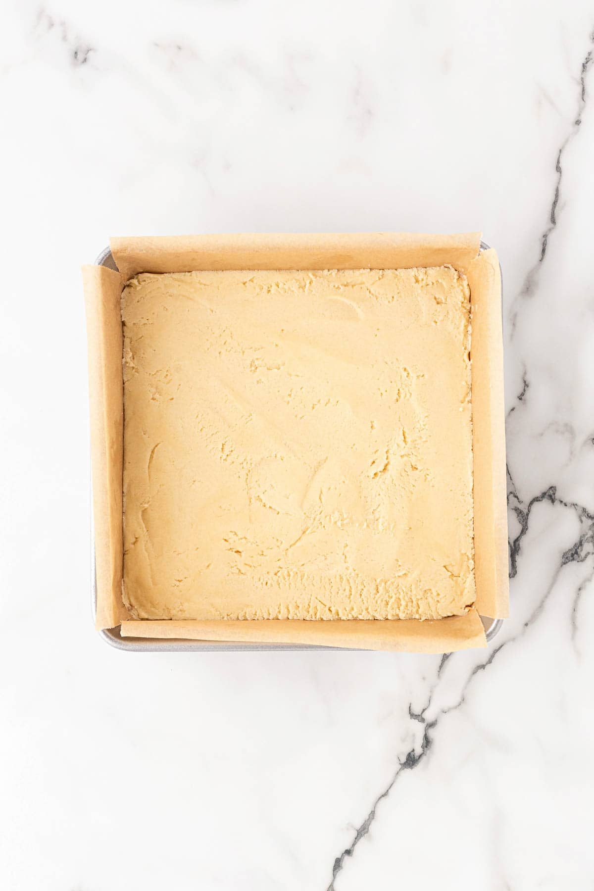 Lemon bar crust pressed evenly into a parchment-lined square baking pan before baking