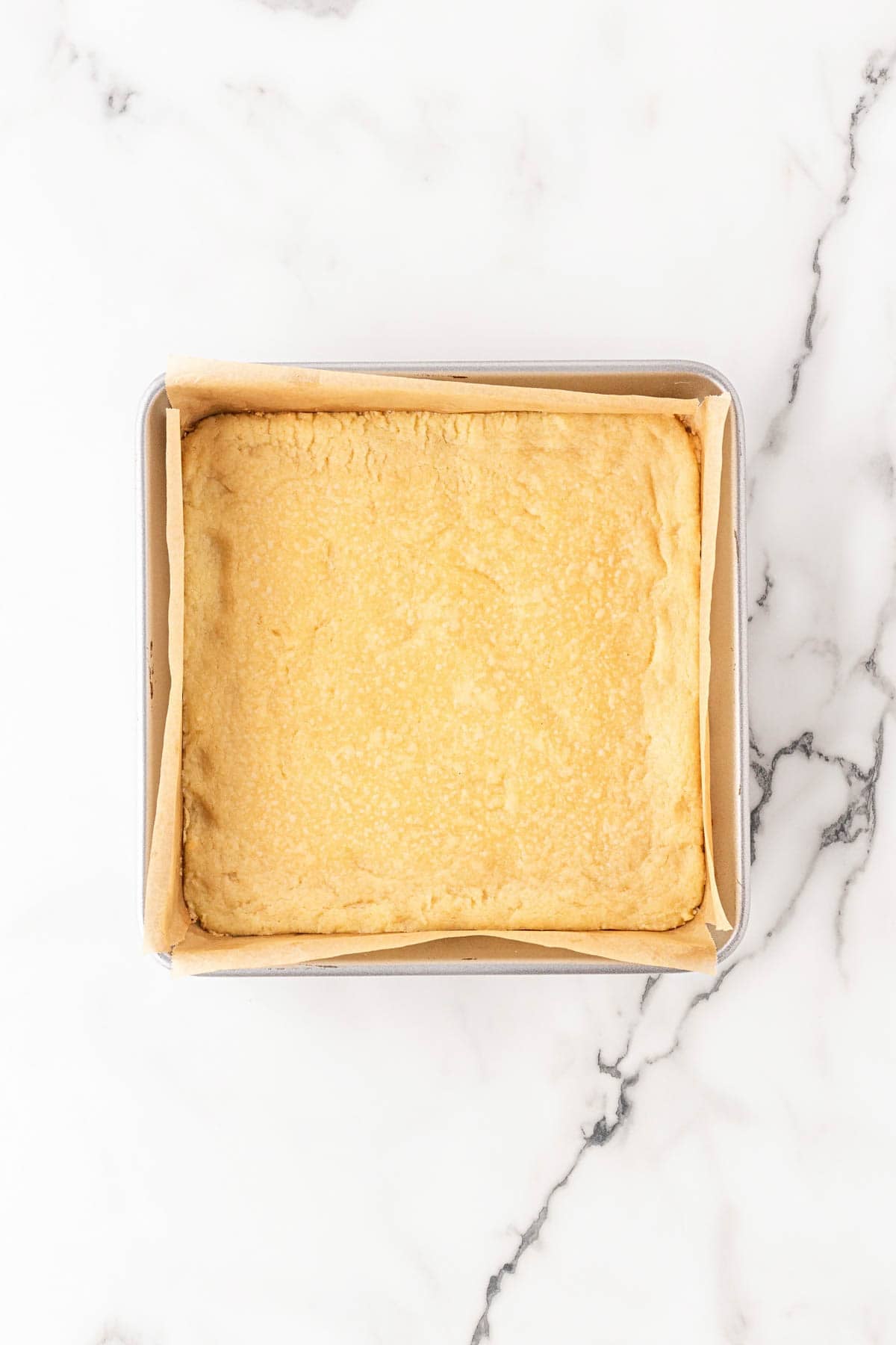 Baked lemon bar crust in a parchment-lined square pan with a lightly golden surface