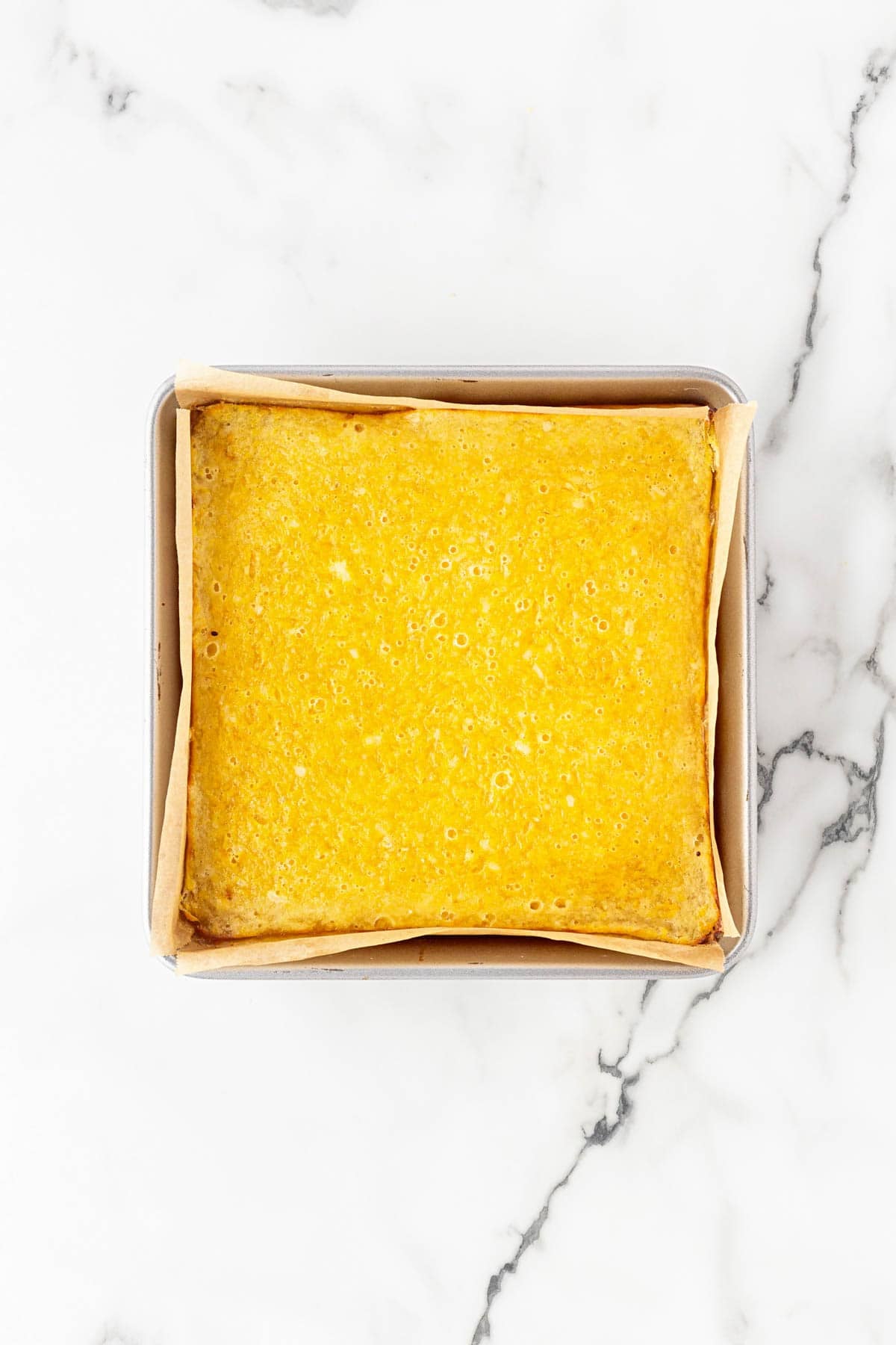 Baked lemon bars cooling in a square pan with a set lemon topping and lightly golden edges