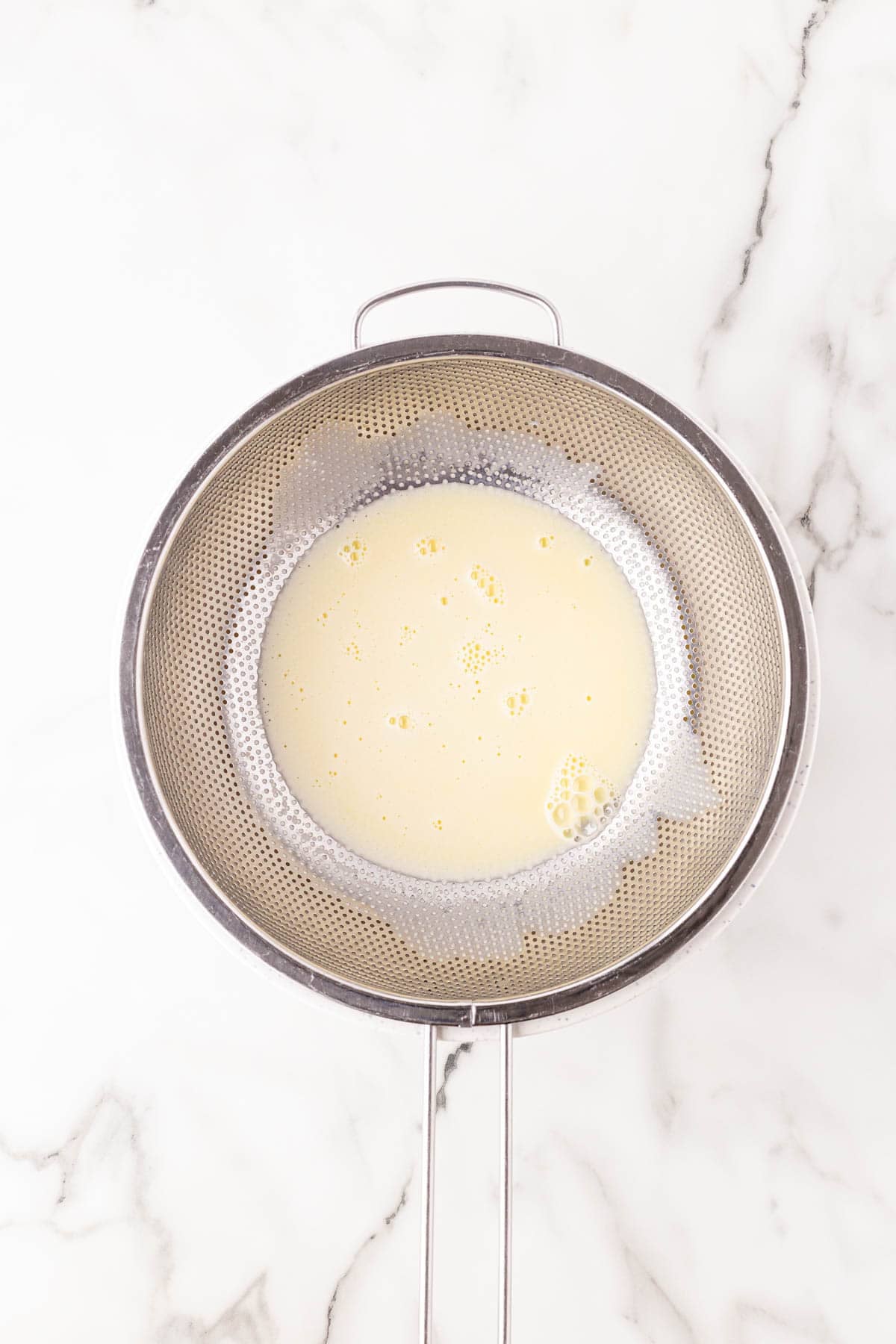 Strained custard base passing through a fine mesh sieve
