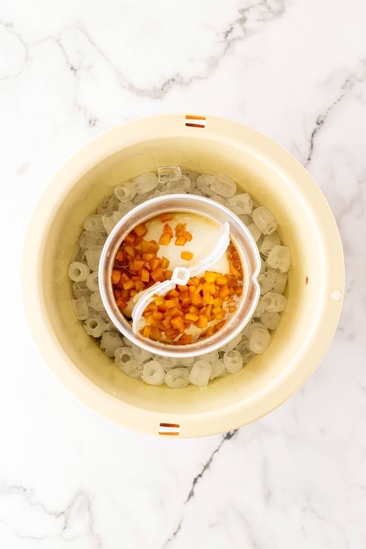 Peach ice cream base churning in an ice cream maker with diced peaches folded in