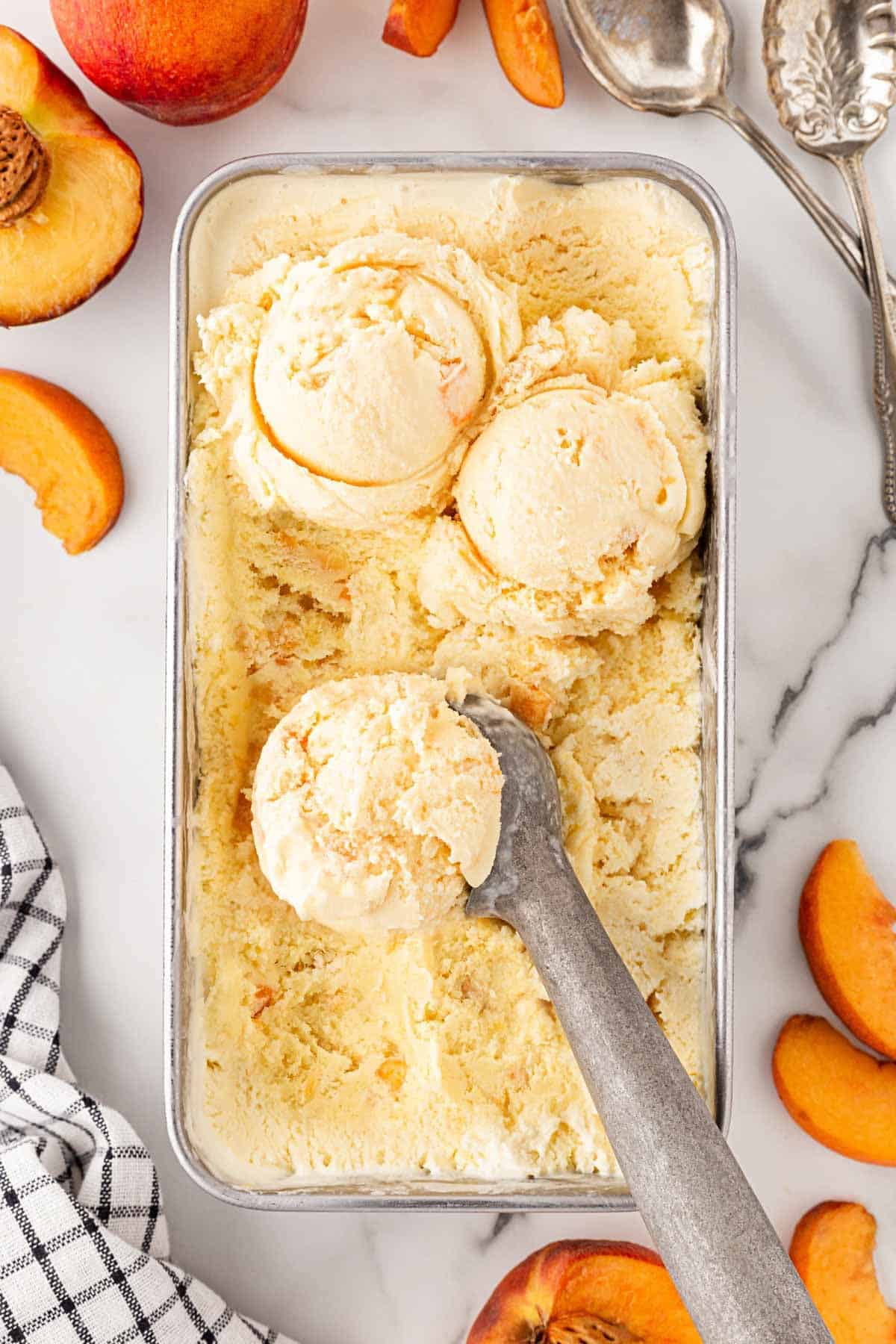 Homemade peach ice cream in a loaf pan with scoops and fresh peach slices