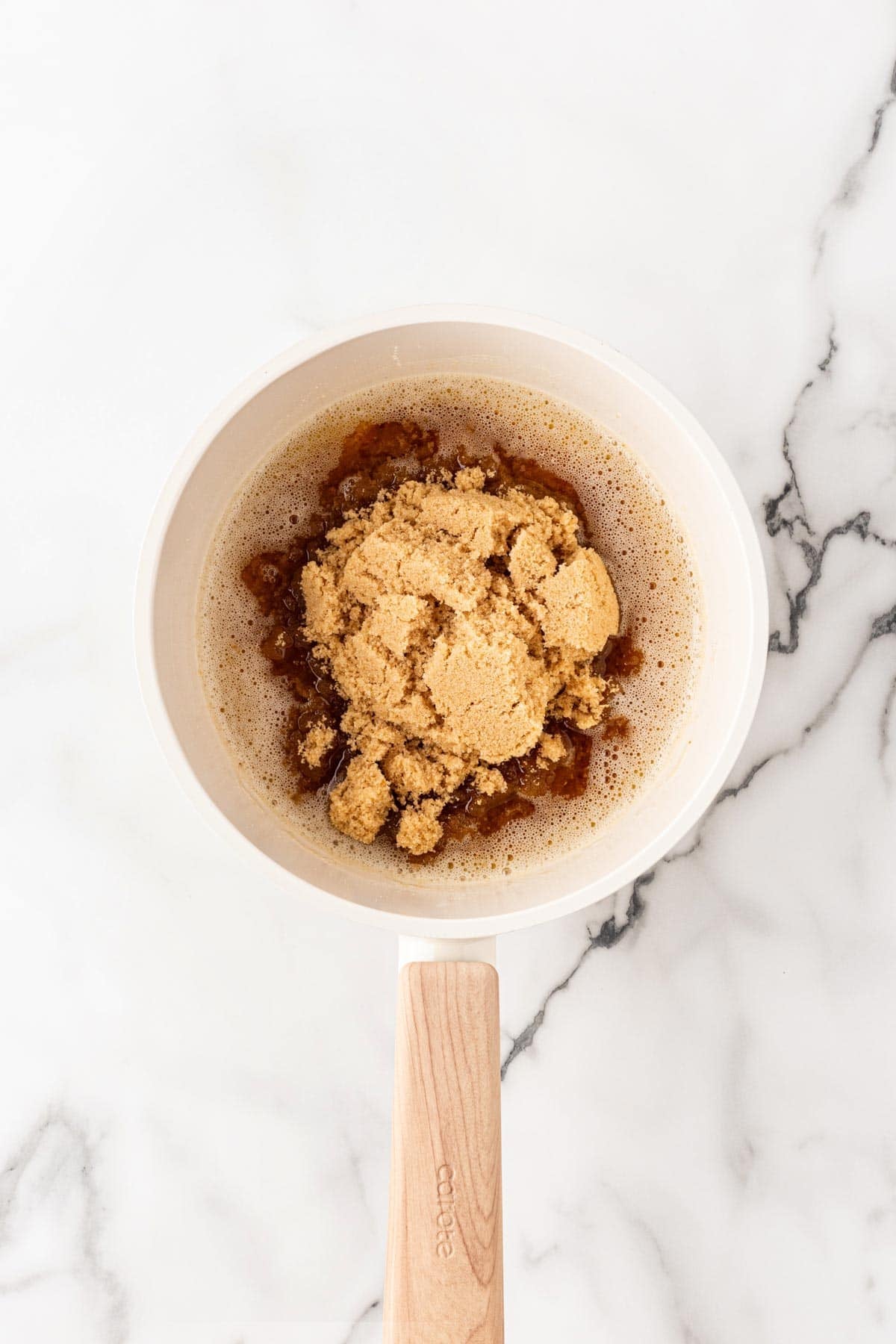 Light brown sugar added to browned butter in a saucepan on a white marble background