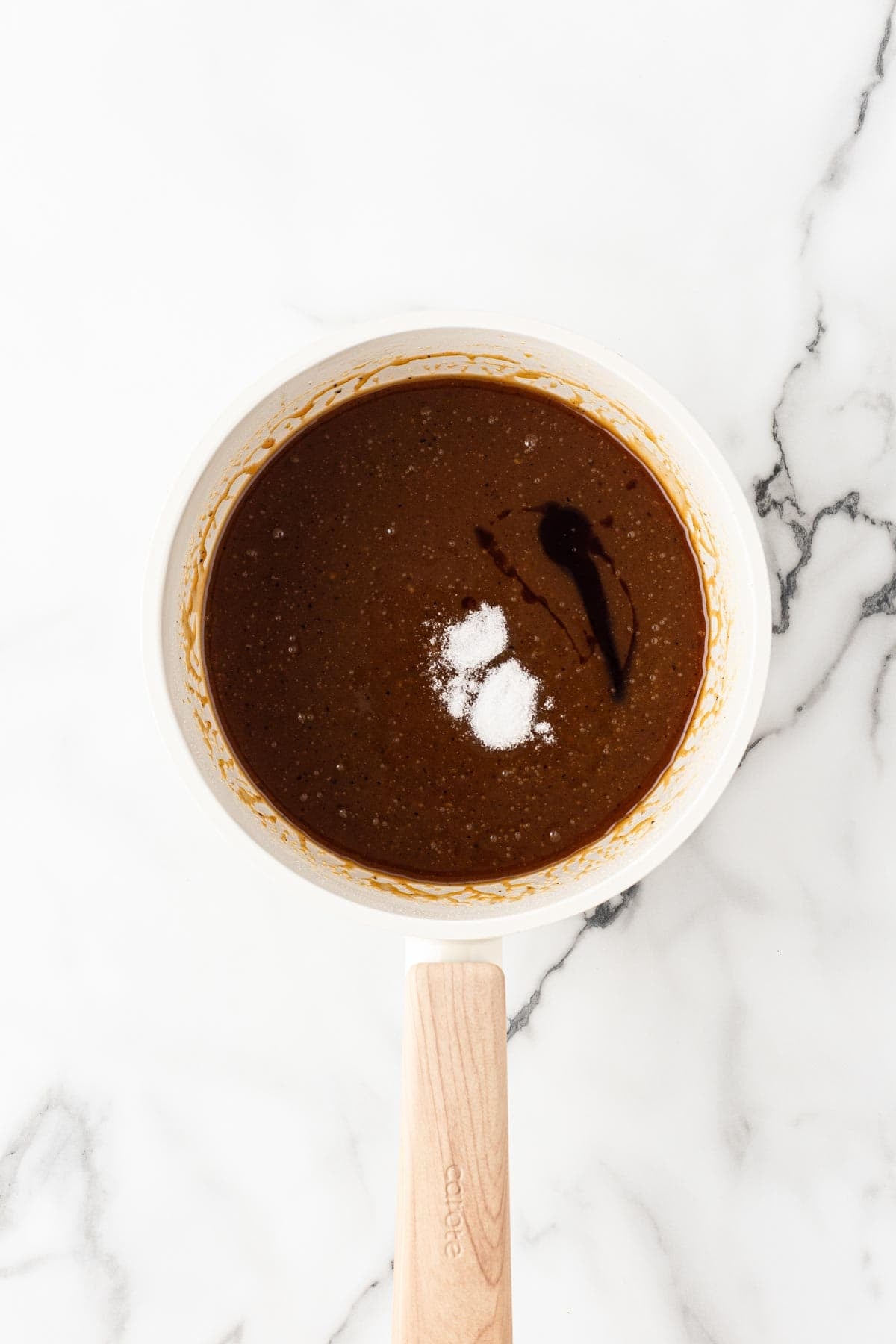 Brown butter caramel mixture with vanilla and salt added in a saucepan on a white marble background