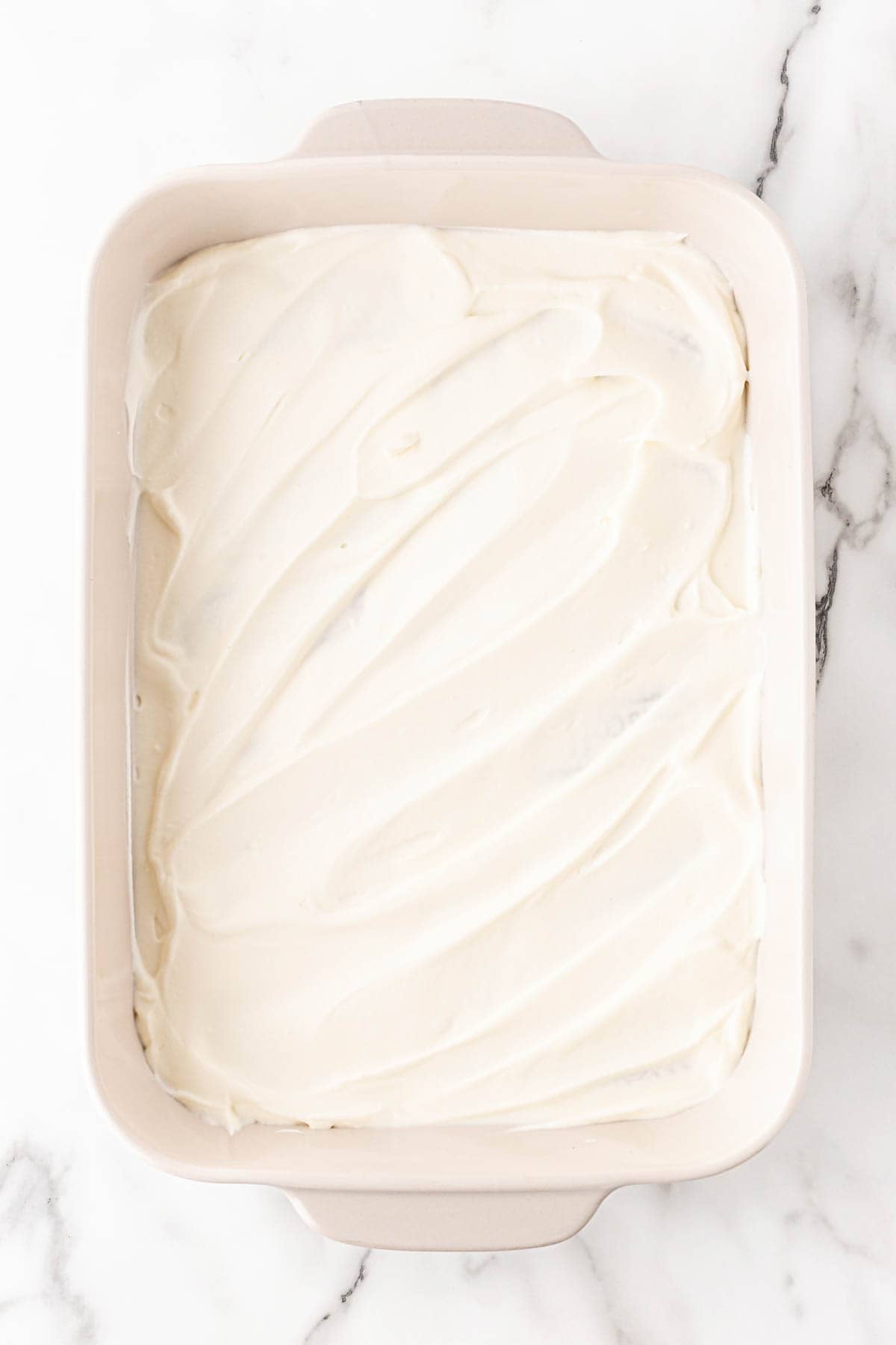 Creamy pudding layer spread evenly over cookies in a baking dish on a white marble background