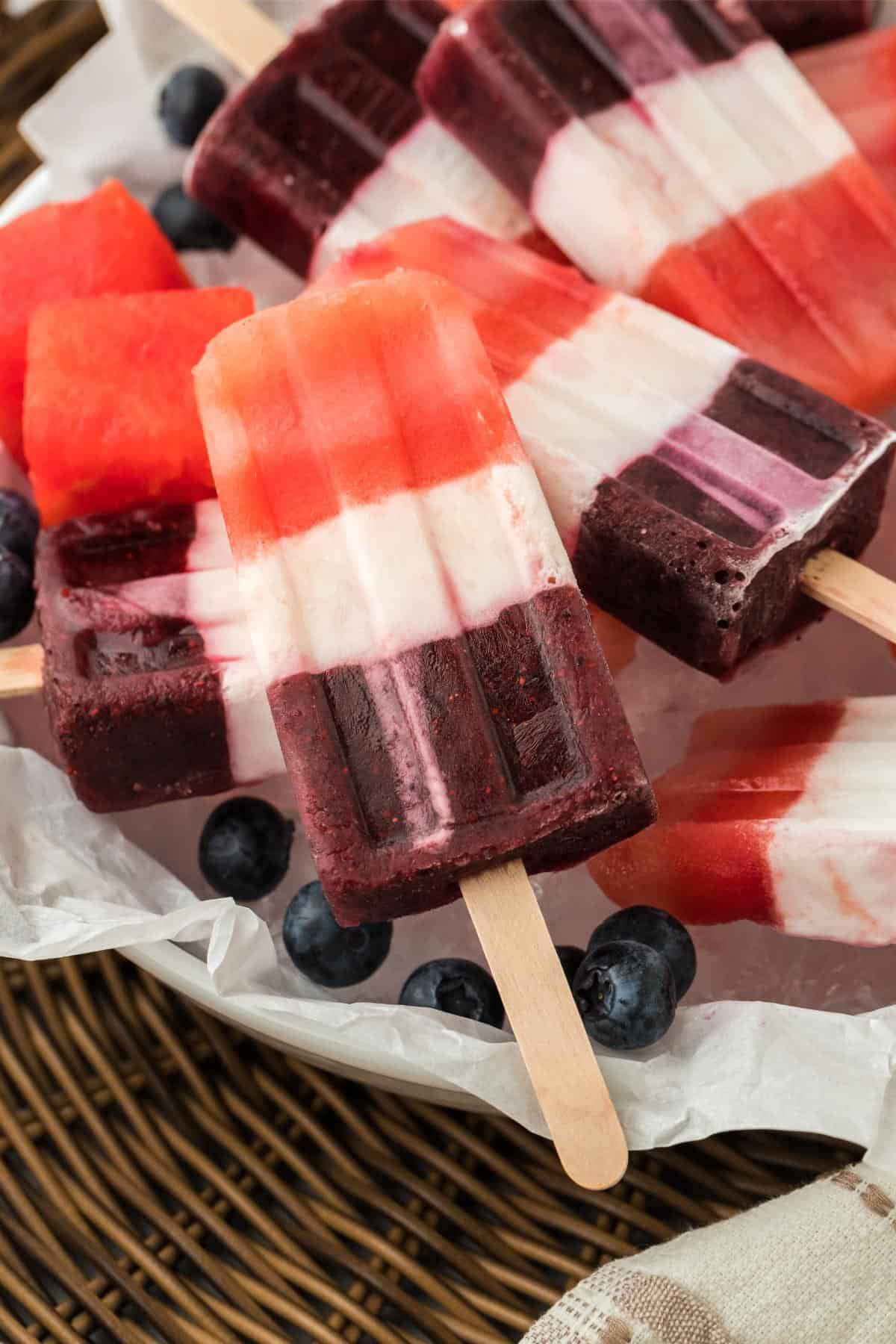 Closeup of red, white, and blue layered popsicles served with fresh blueberries