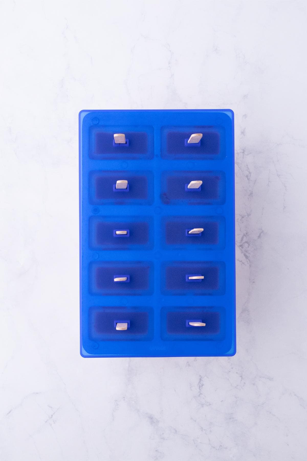 Blue popsicle mold filled with layered popsicle mixture and wooden sticks inserted