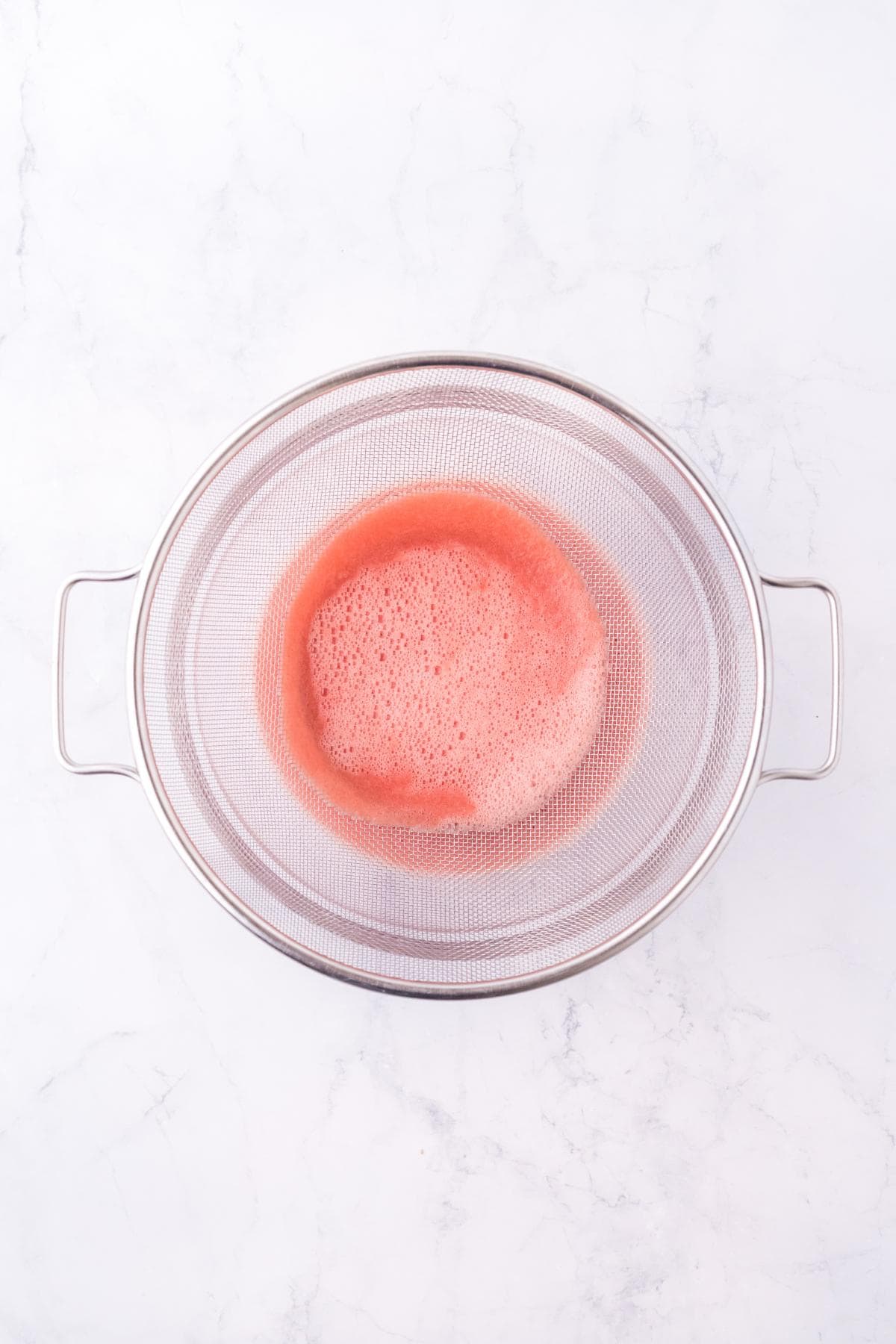 Strained watermelon puree in a fine mesh sieve