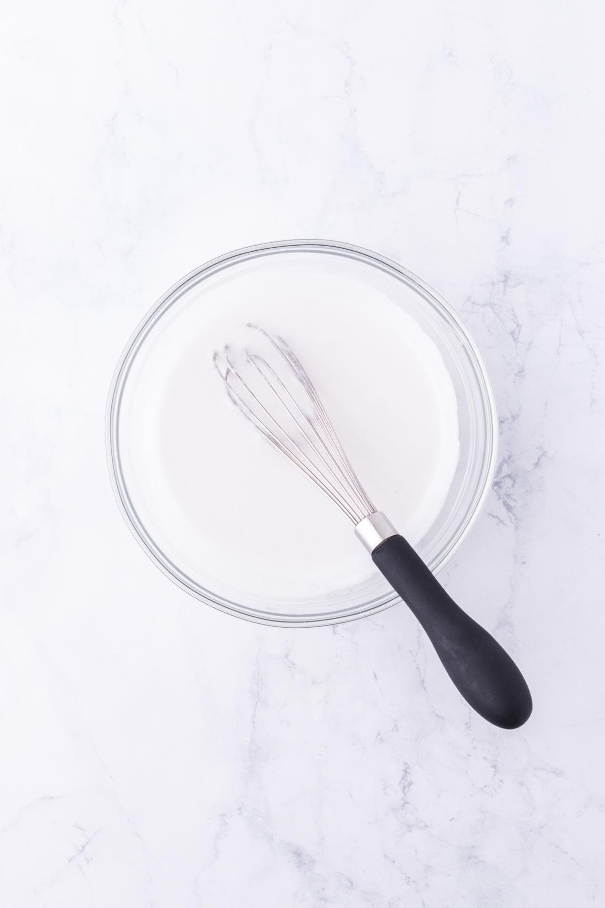 Glass mixing bowl with a whisk and creamy white popsicle mixture
