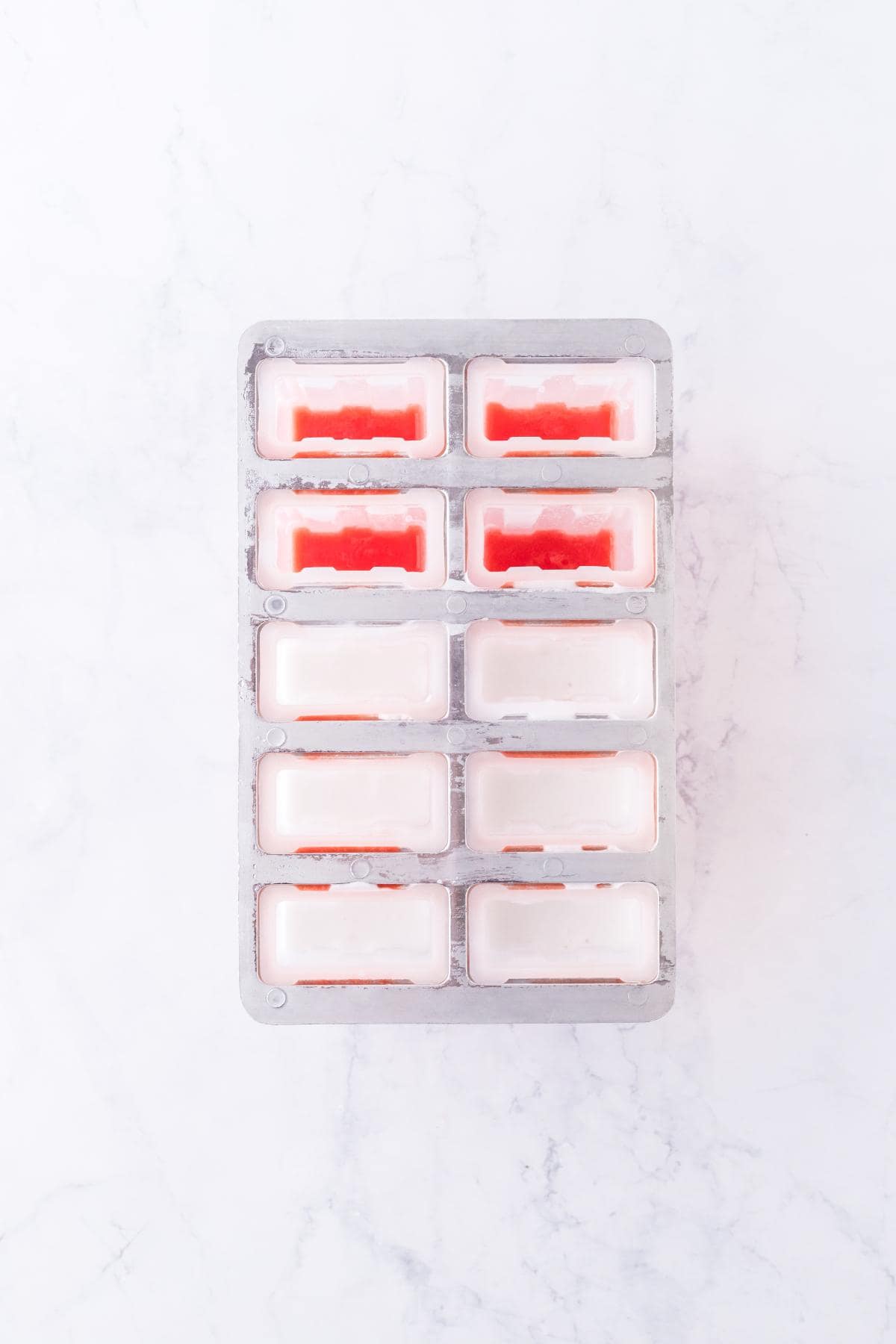 Popsicle mold with frozen watermelon layer and white cream layer added