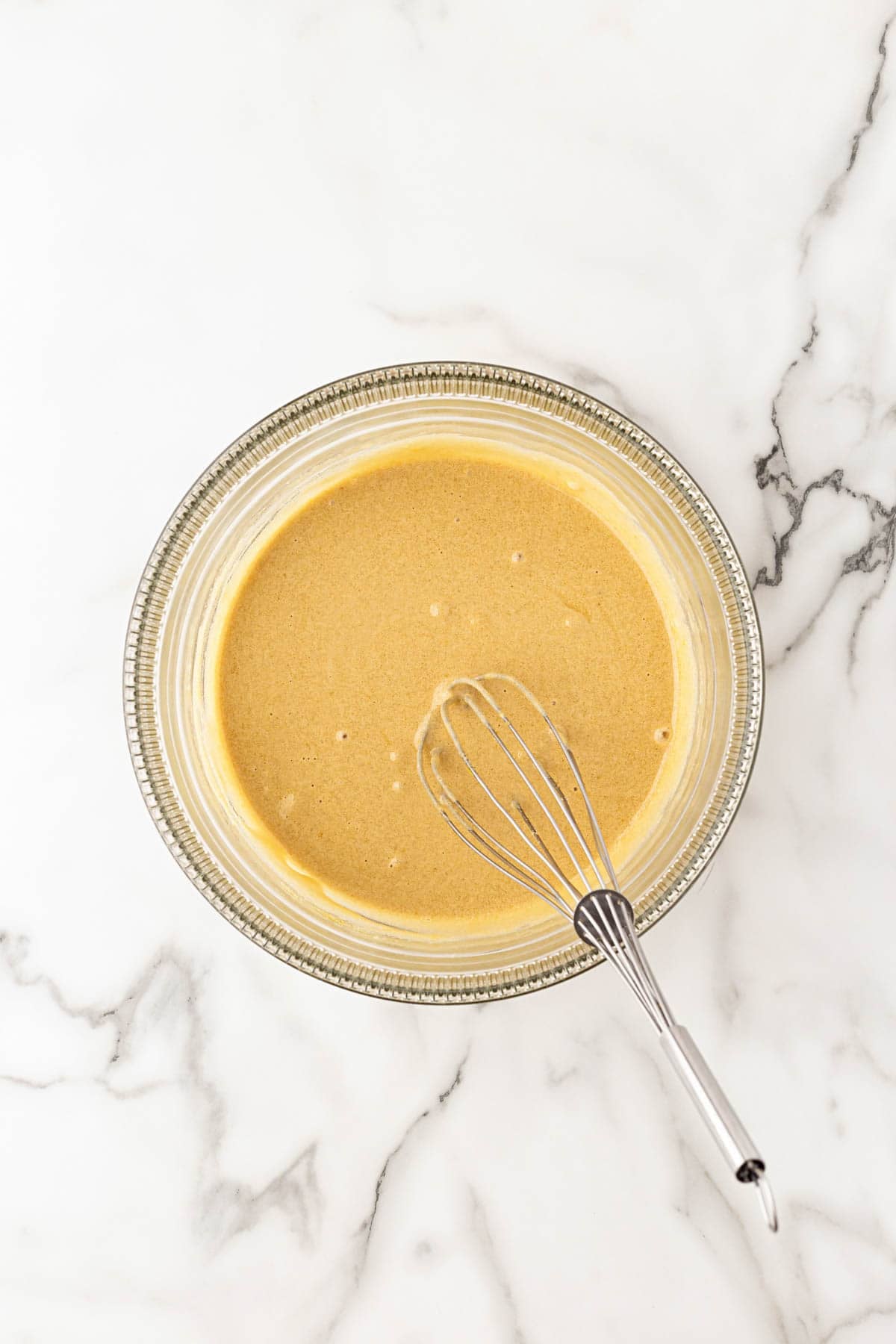 Eggs, egg yolks, brown sugar, and granulated sugar whisked together in a glass bowl on a white marble countertop