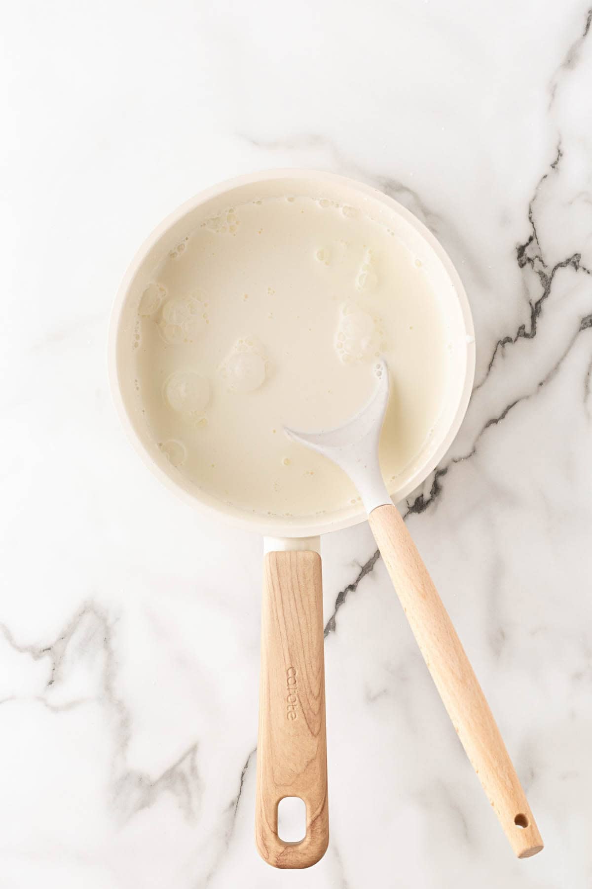 Heavy cream, half-and-half, and salt heating in a white saucepan on a white marble countertop