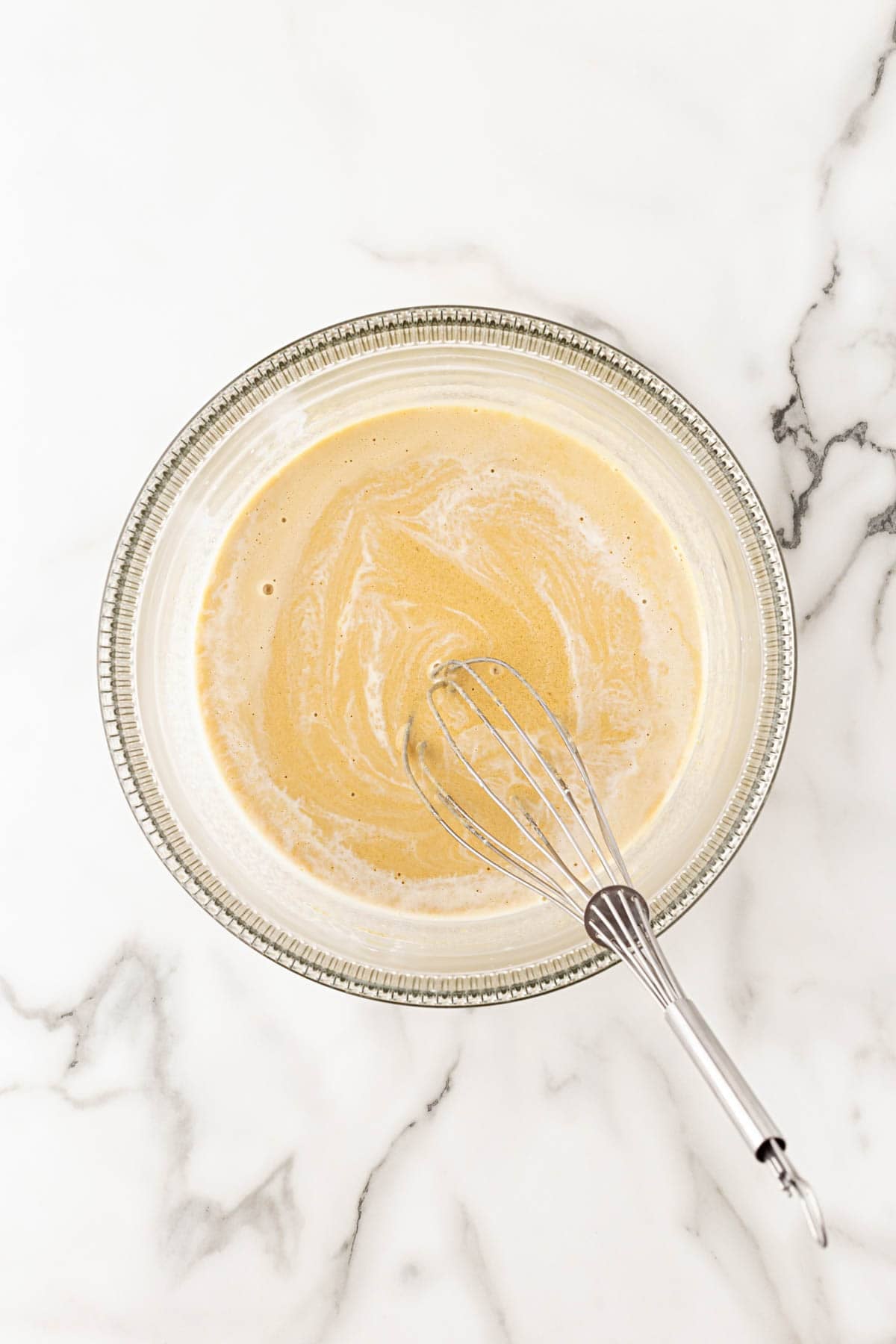 Hot cream whisked into the egg and sugar mixture to temper the eggs in a glass bowl on a marble countertop