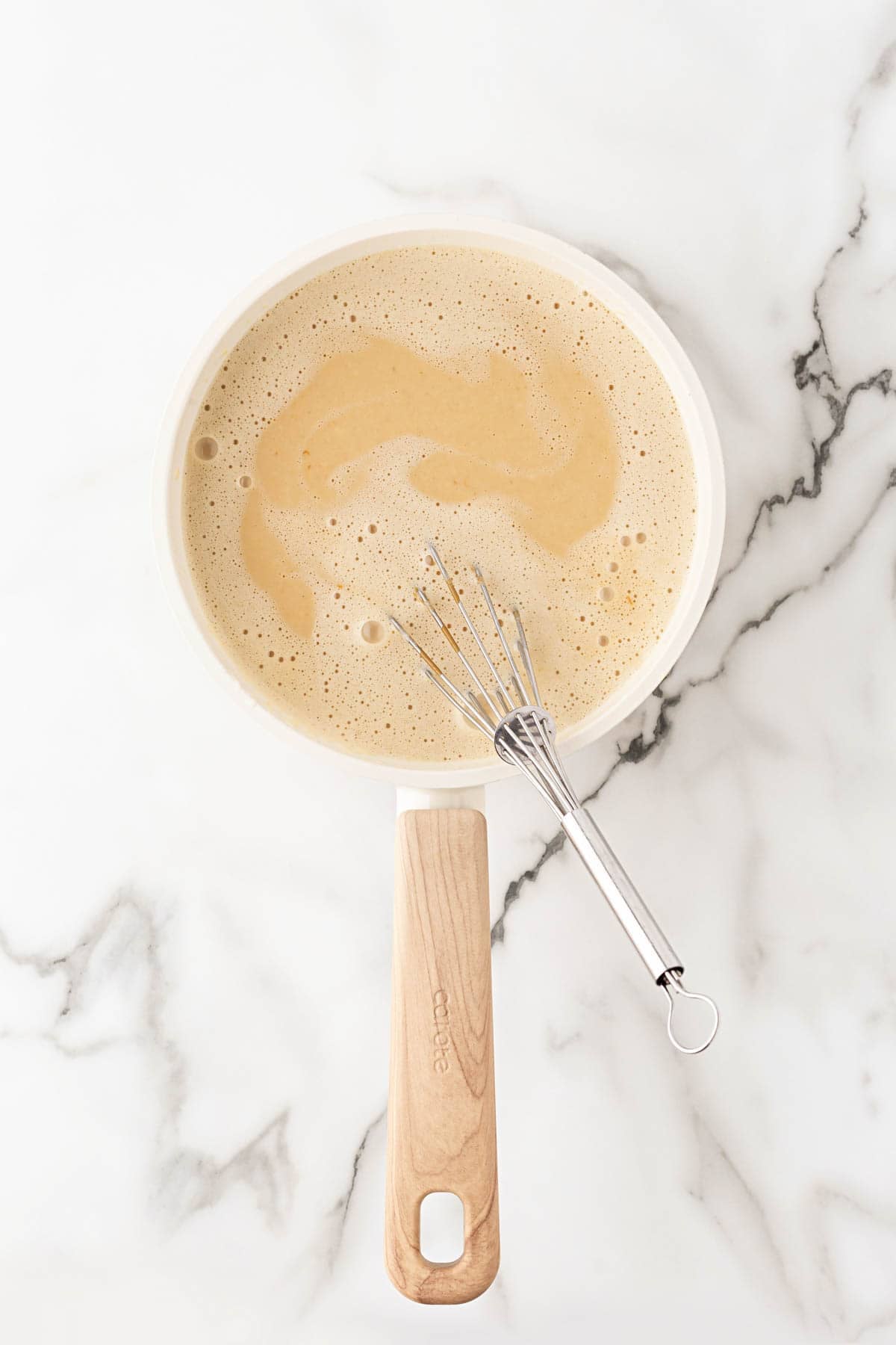 Biscoff cookie butter and vanilla whisked into the cooked ice cream custard in a saucepan on a marble countertop