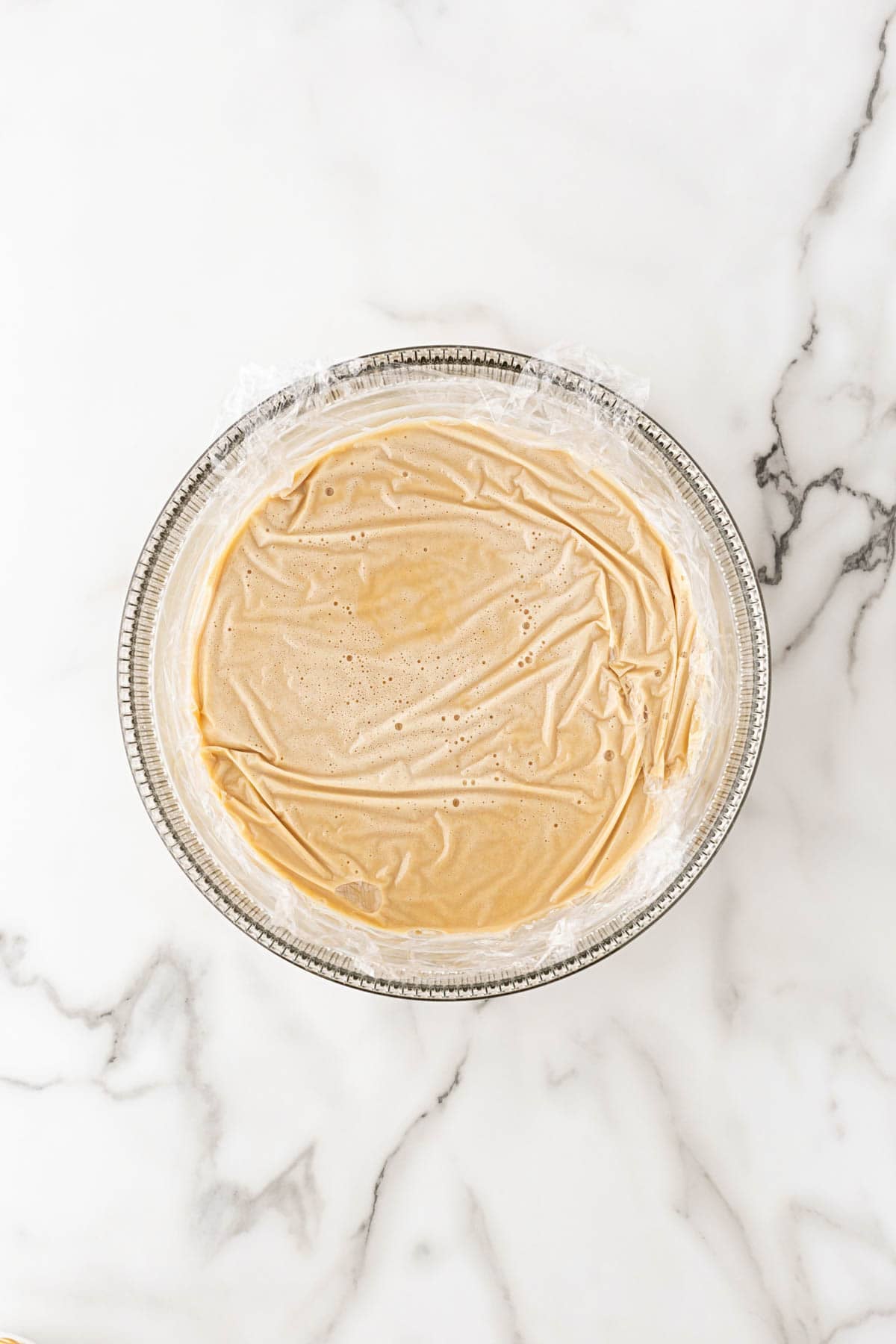 Biscoff ice cream custard covered directly with plastic wrap in a glass bowl before chilling