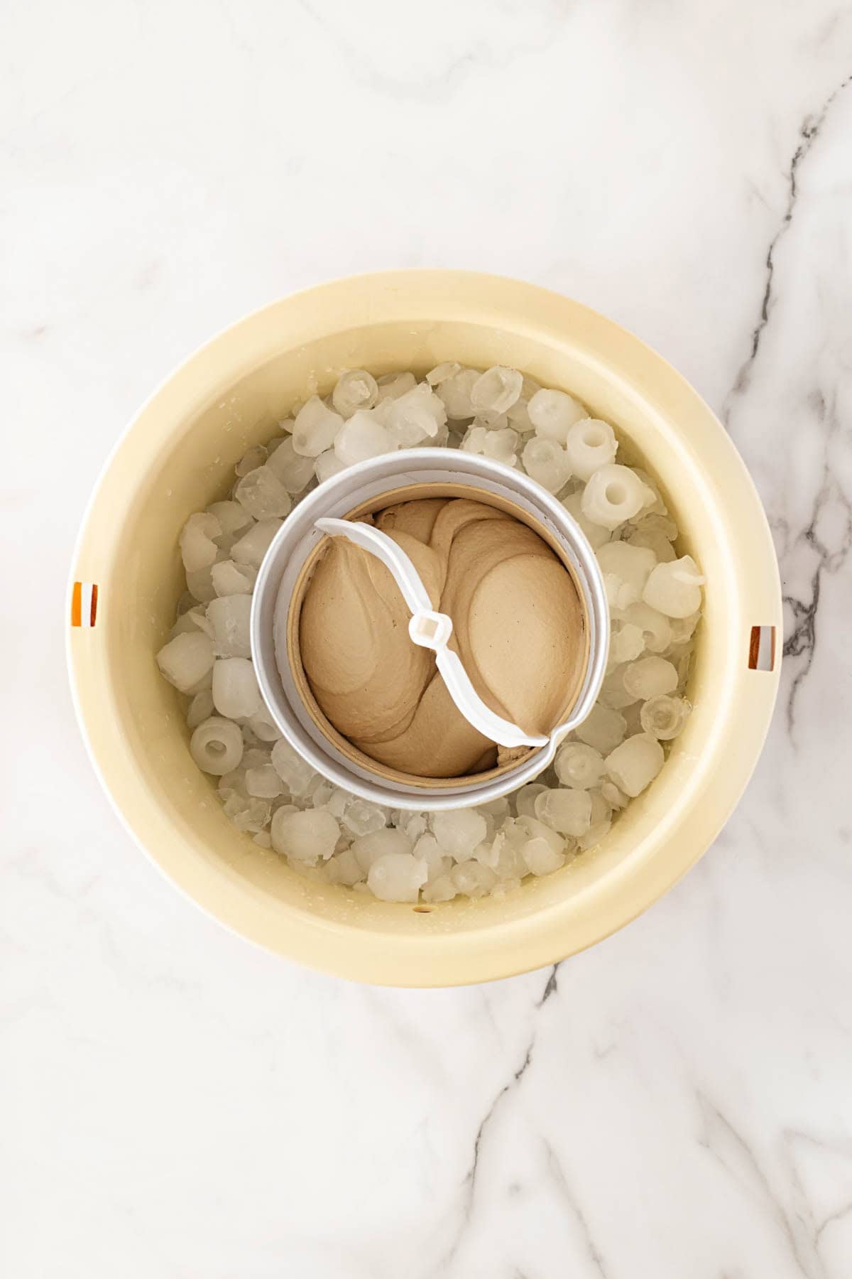 Biscoff ice cream custard churning in an ice cream maker surrounded by ice on a white marble countertop