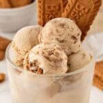 Scoops of Biscoff ice cream in a glass dessert cup topped with Biscoff cookies, with more cookies in the background