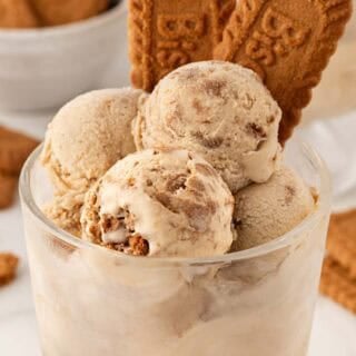 Scoops of Biscoff ice cream in a glass dessert cup topped with Biscoff cookies, with more cookies in the background