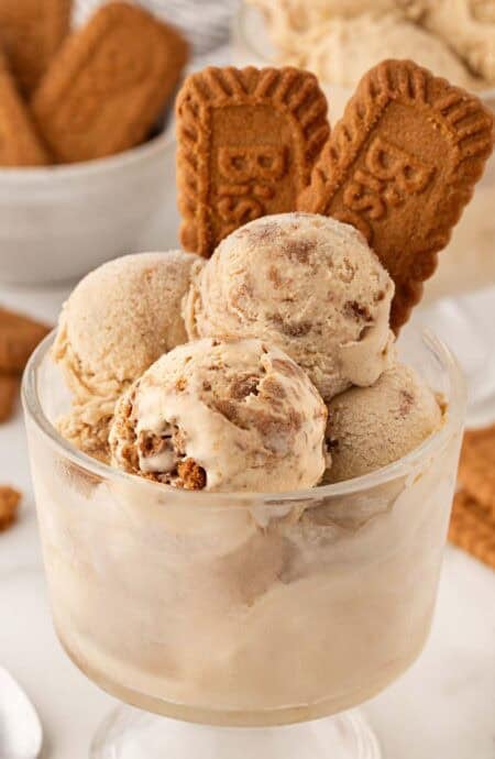 Scoops of Biscoff ice cream in a glass dessert cup topped with Biscoff cookies, with more cookies in the background