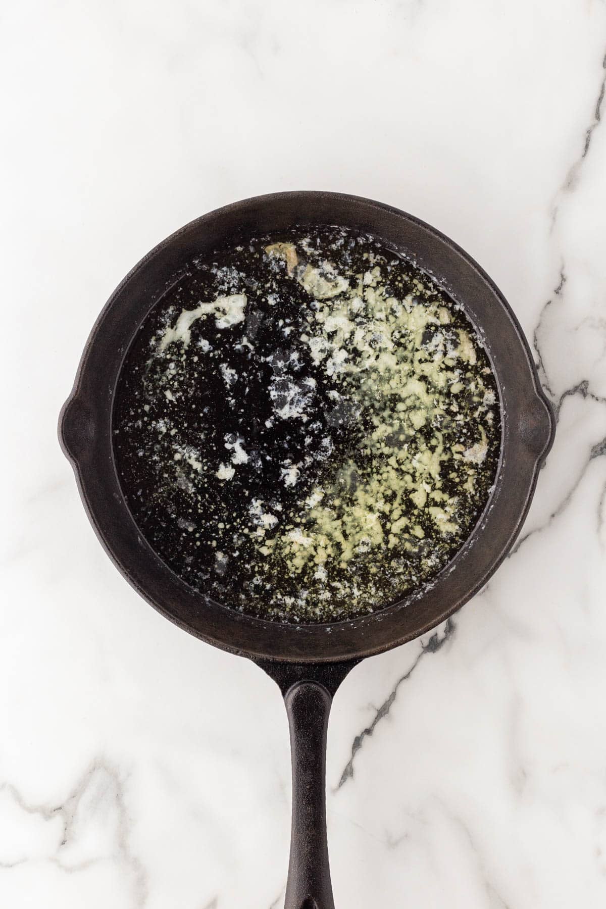 Melted butter in a cast iron skillet on a white marble countertop