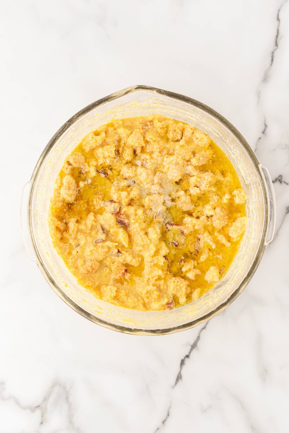 Cornbread batter with pork cracklings and bacon mixed together in a glass bowl on a white marble countertop