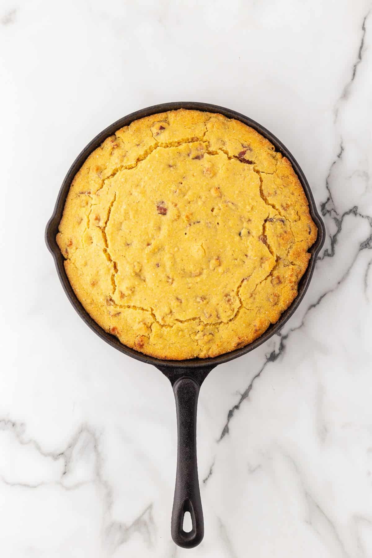 Freshly baked crackling cornbread in a cast iron skillet on a white marble countertop