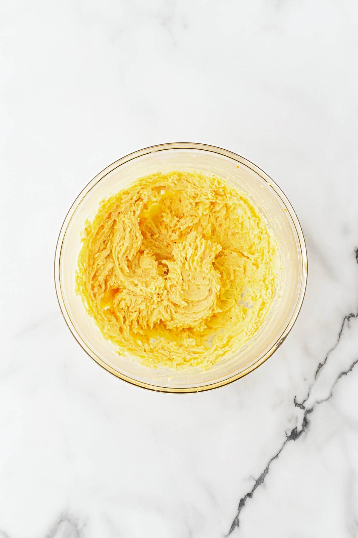 Creamed butter, sugar, and orange zest mixture in a glass bowl on a white marble countertop