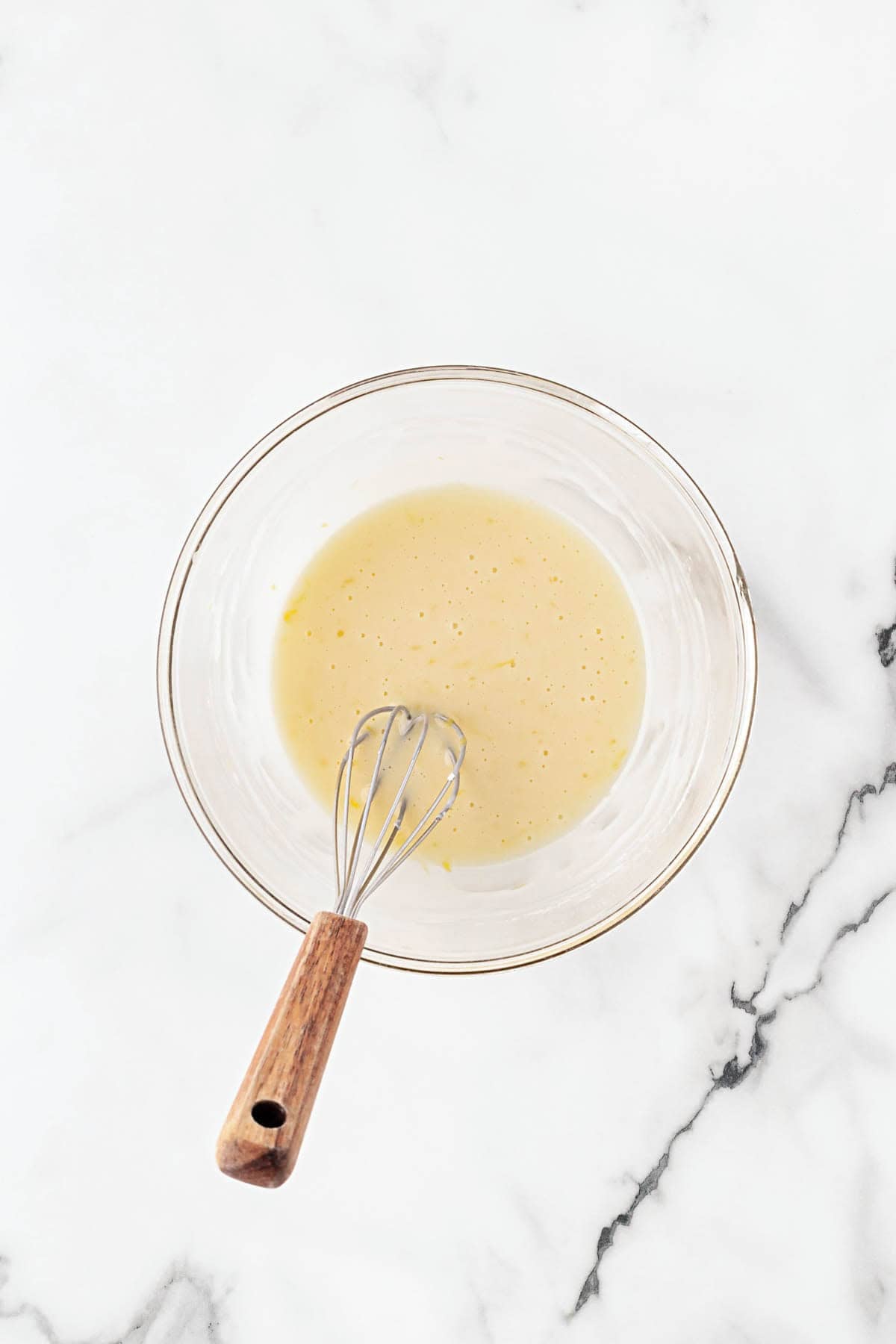 Orange glaze whisked smooth in a glass bowl on a white marble countertop