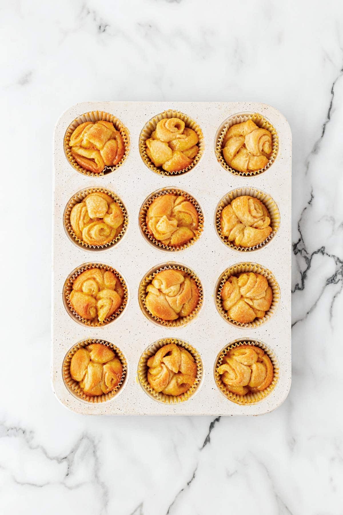 Freshly baked orange rolls in a paper-lined muffin pan on a white marble countertop