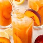 peach cobbler lemonade with peach slices and ice in a tall glass.