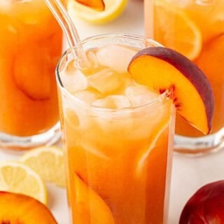 peach cobbler lemonade with peach slices and ice in a tall glass.