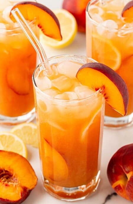 peach cobbler lemonade with peach slices and ice in a tall glass.