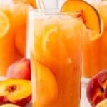 peach cobbler lemonade with peach slices and ice in a tall glass.