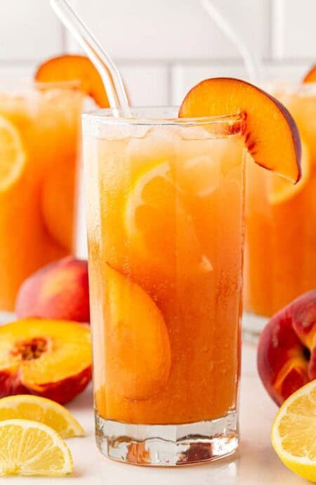 peach cobbler lemonade with peach slices and ice in a tall glass.
