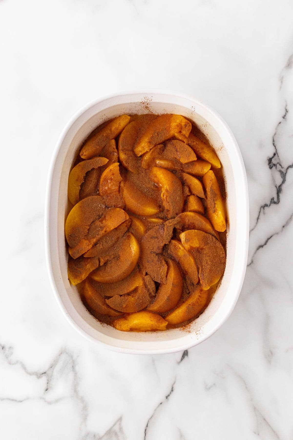Sliced peaches sprinkled with apple pie spice in a white baking dish