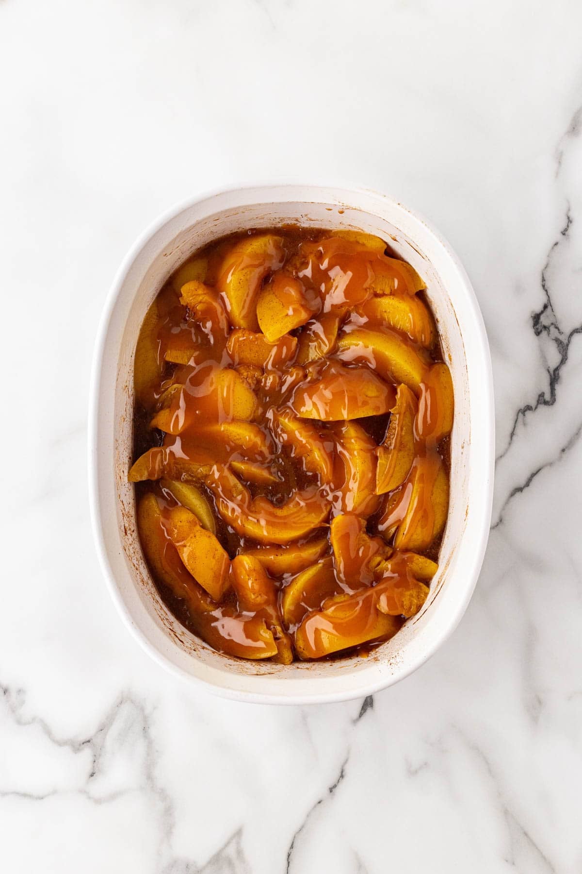 Spiced peaches drizzled with caramel sauce in a white baking dish