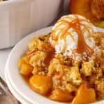 Peach dump cake topped with vanilla ice cream and caramel sauce, served in a white bowl