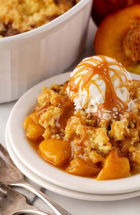 Peach dump cake topped with vanilla ice cream and caramel sauce, served in a white bowl
