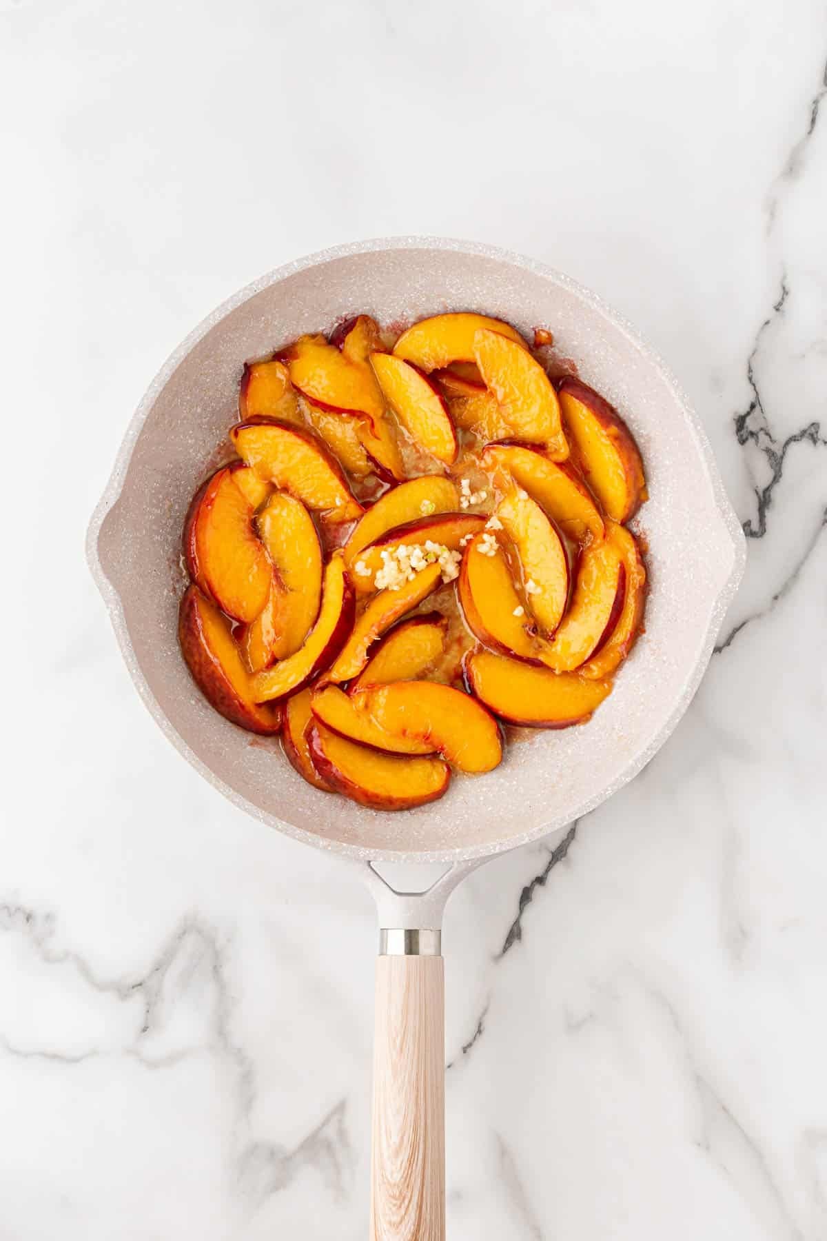Fresh peach slices cooking with butter, brown sugar, and garlic in a skillet