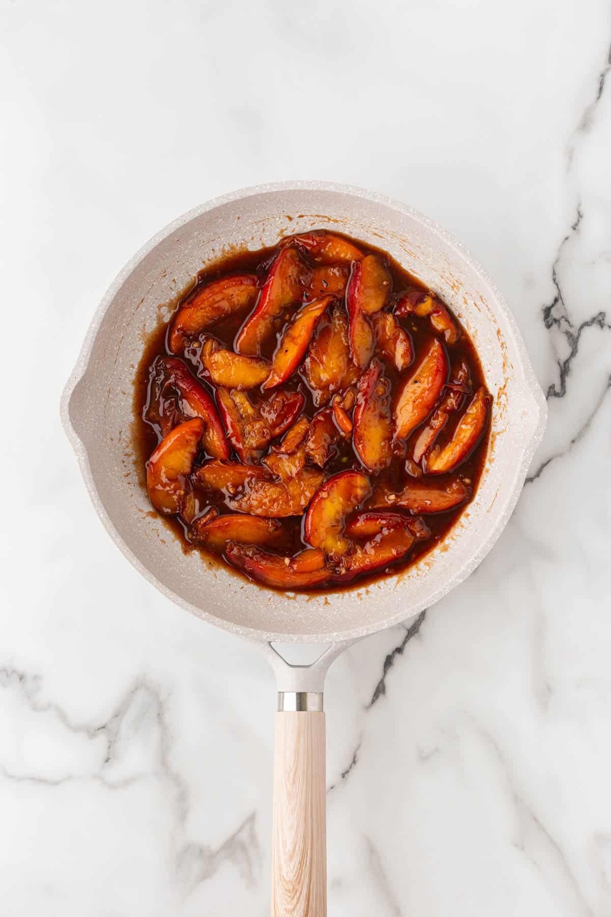 Peach glaze simmering with sliced peaches in a skillet