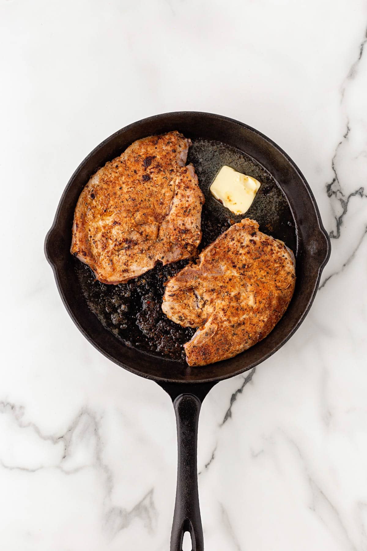 Seasoned pork chops searing in a cast iron skillet with butter