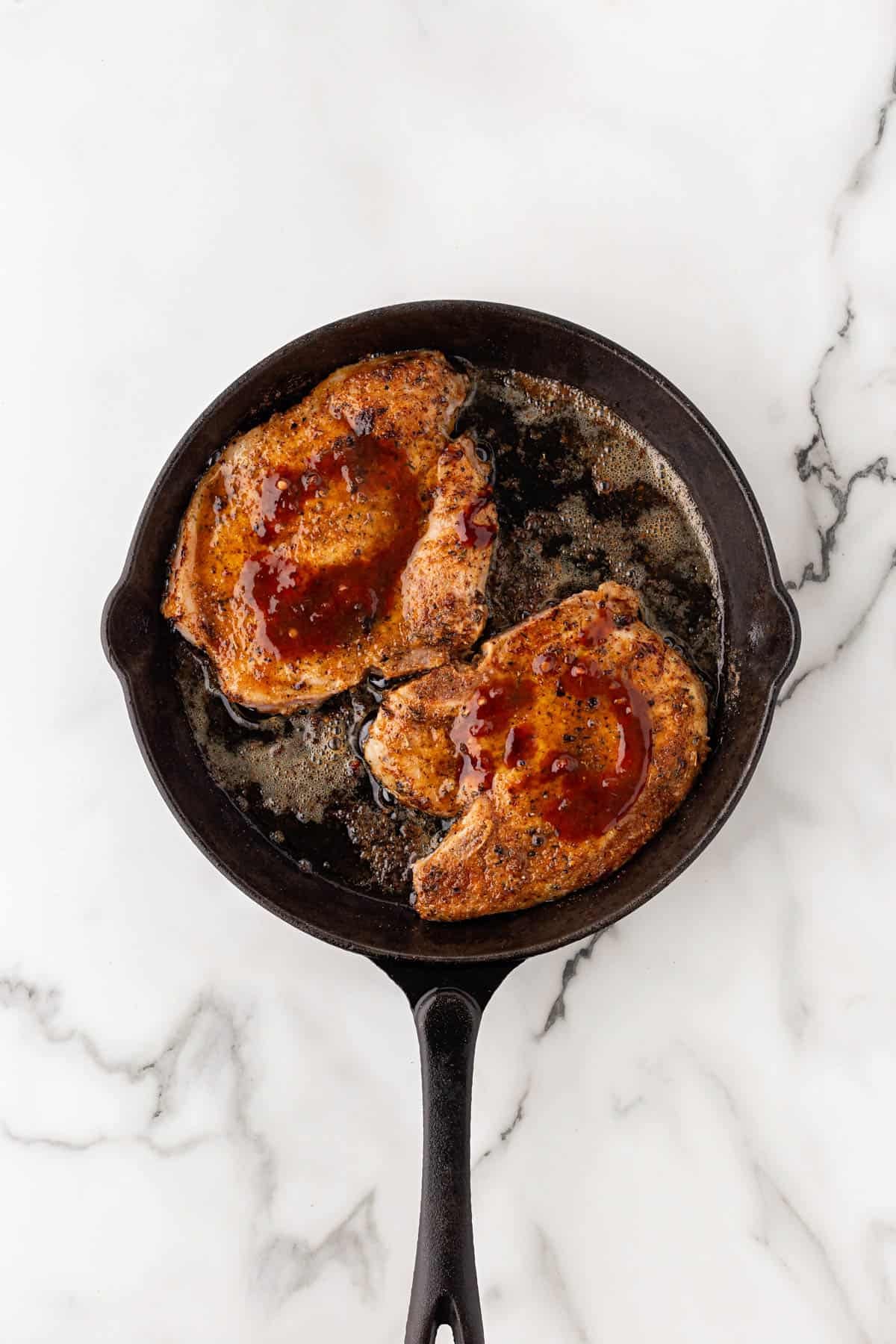 Pork chops topped with peach glaze in a cast iron skillet