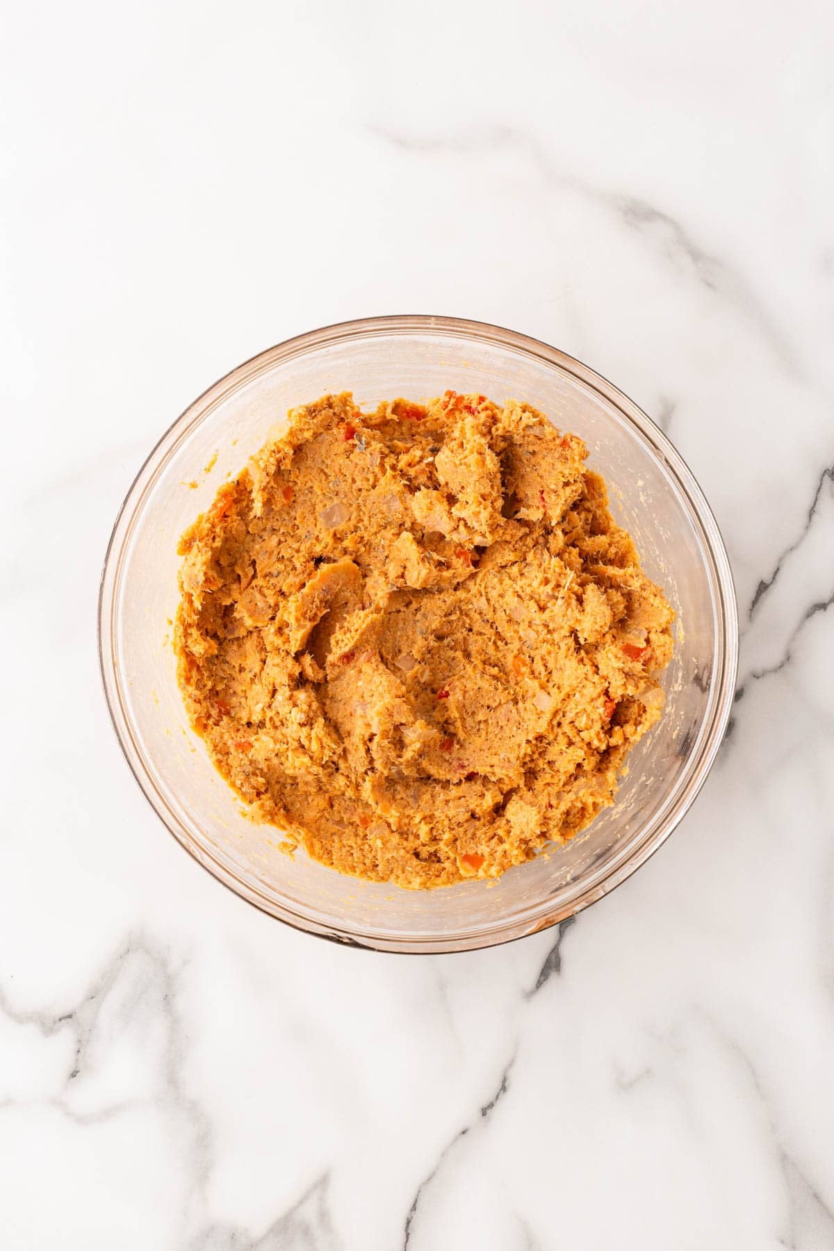 Salmon cake mixture in a clear glass bowl on a white marble countertop