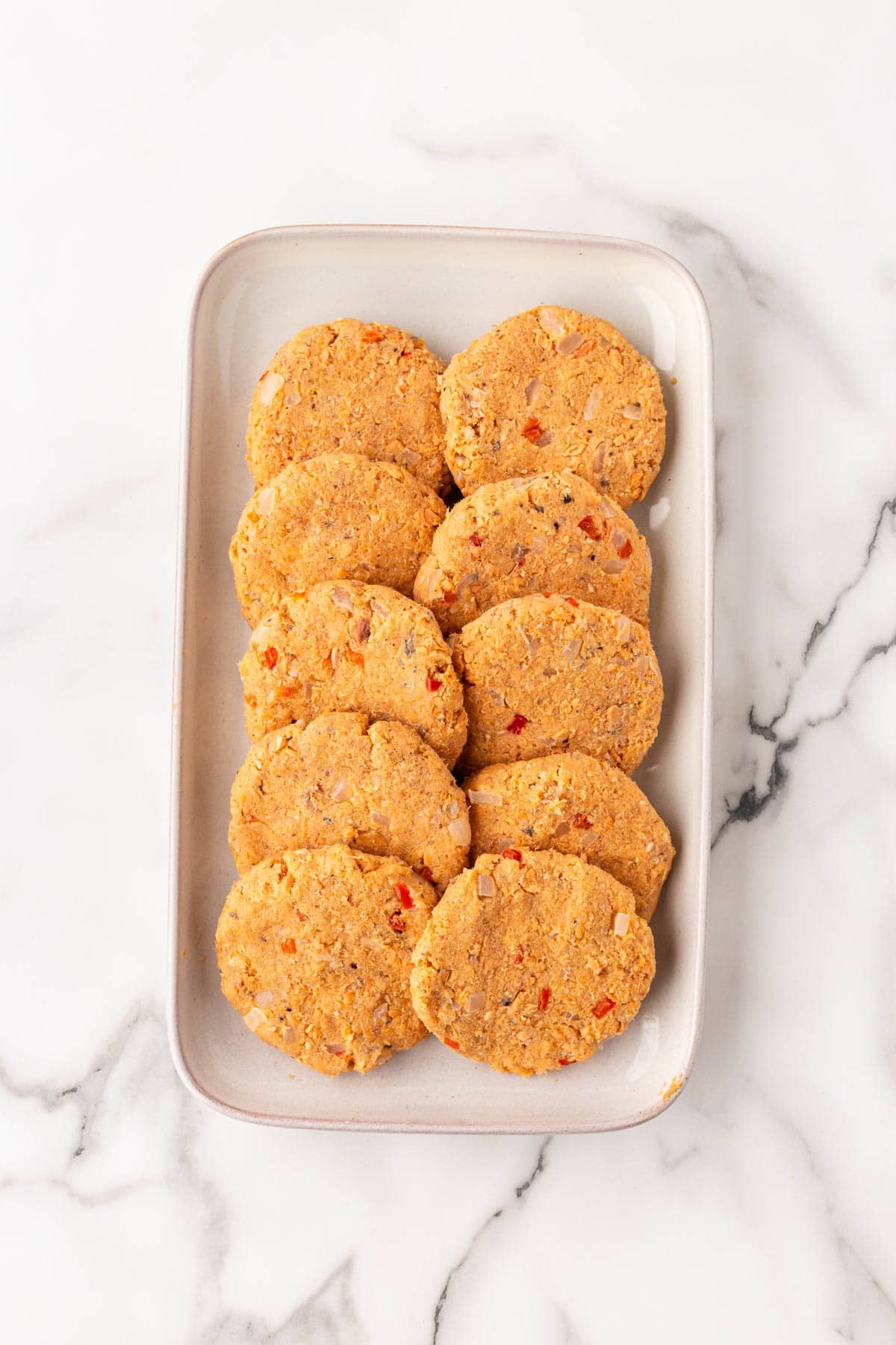 Uncooked salmon cakes arranged on a rectangular platter on a white marble countertop