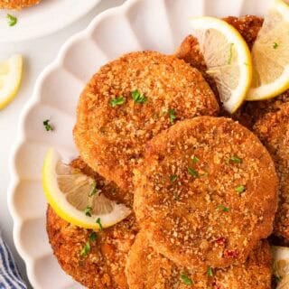 Overhead shot of crispy salmon cakes garnished with parsley and lemon wedges on a white serving platter, with black pepper and extra salmon cakes in the background
